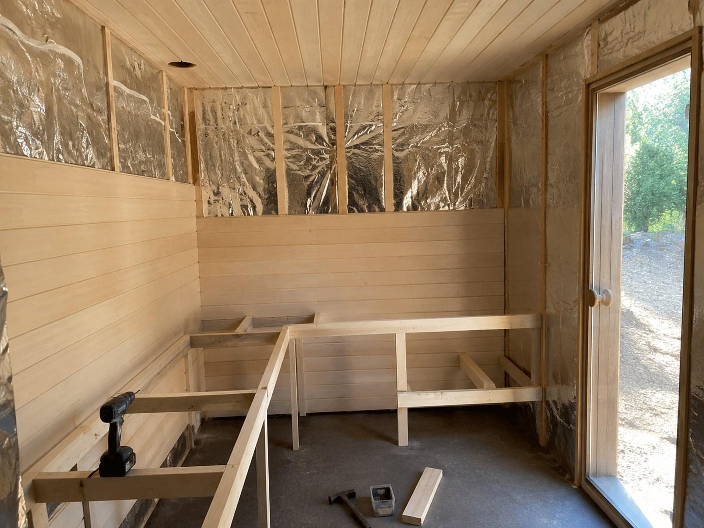 Sauna under construction with foil, aspen panelling and bench frame