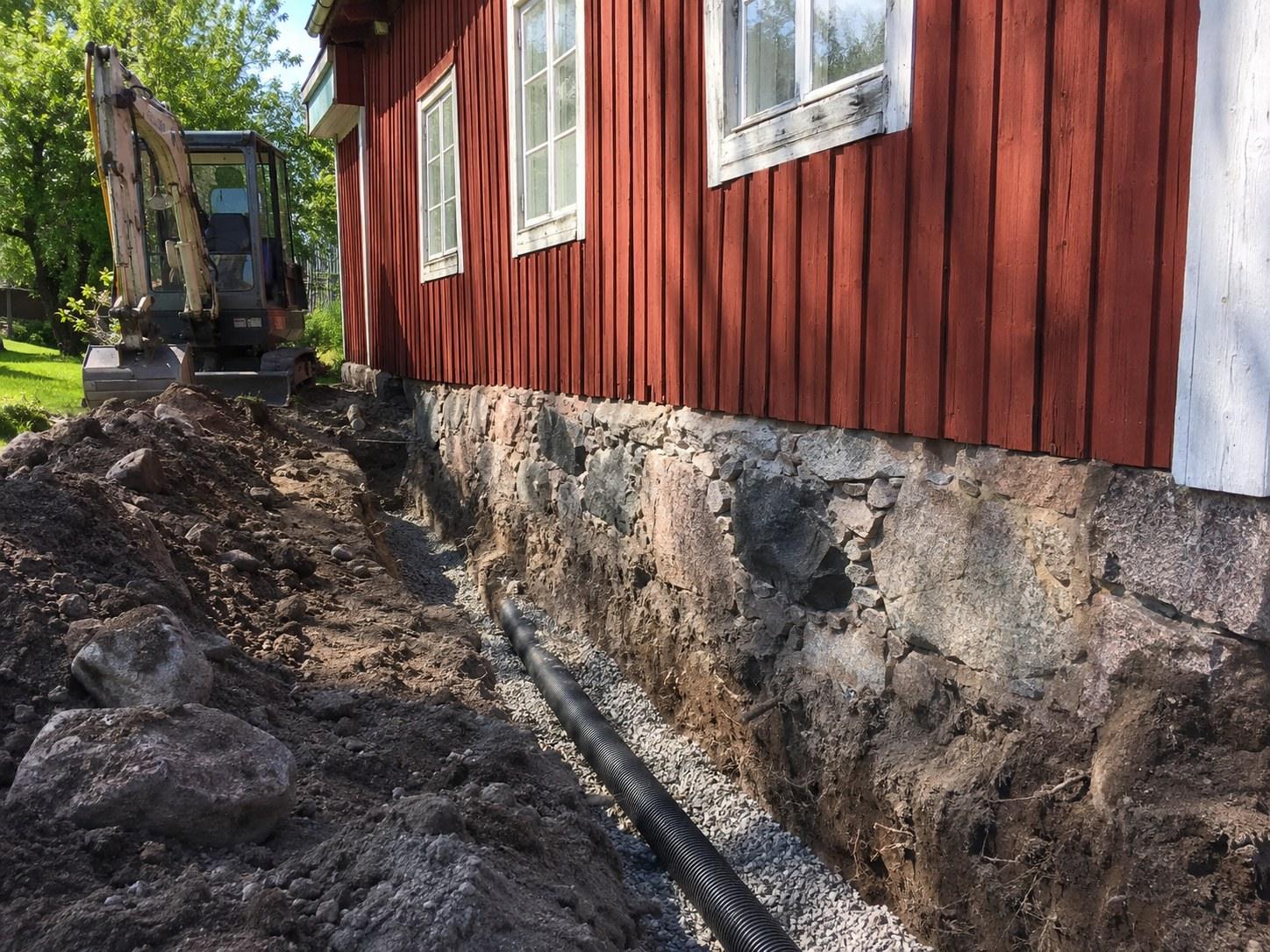 Excavator and drainage pipe along the stone foundation of a red house