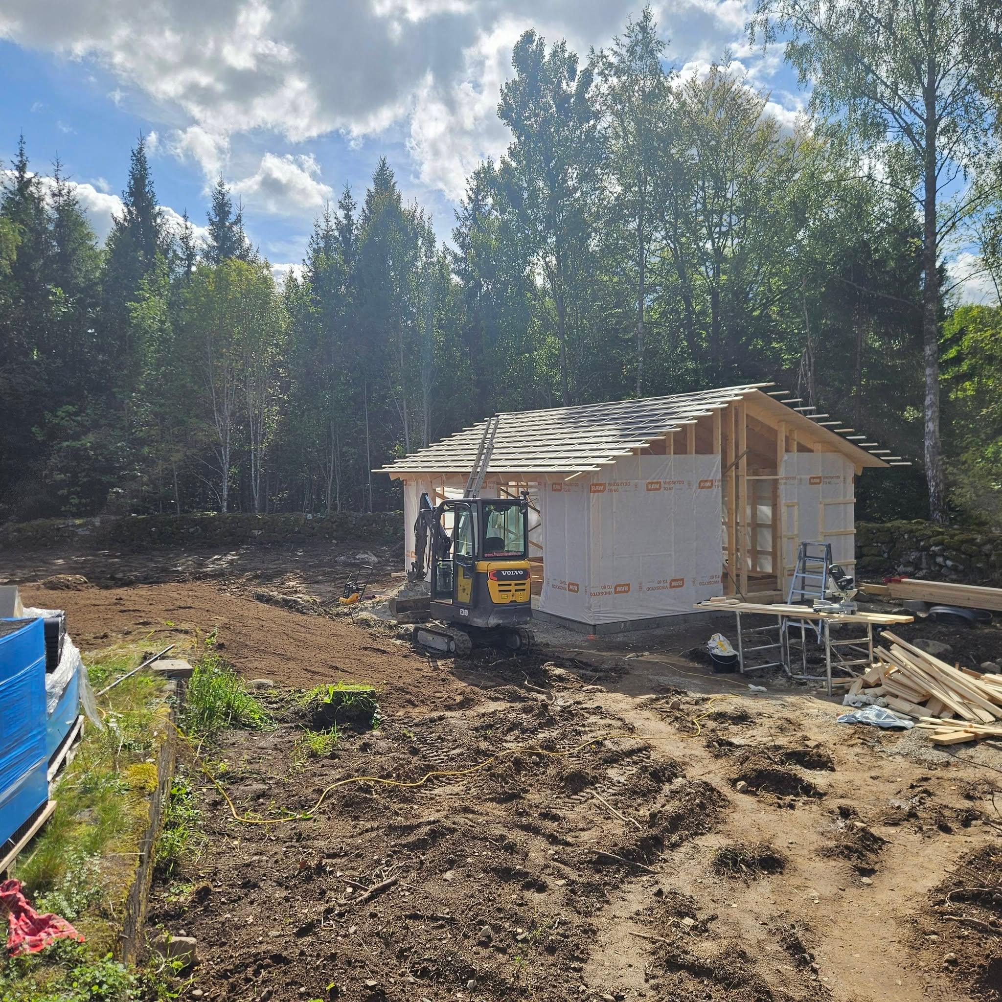 Attefallshuset med takstolar, läkt och vindskydd på plats, grävmaskin intill