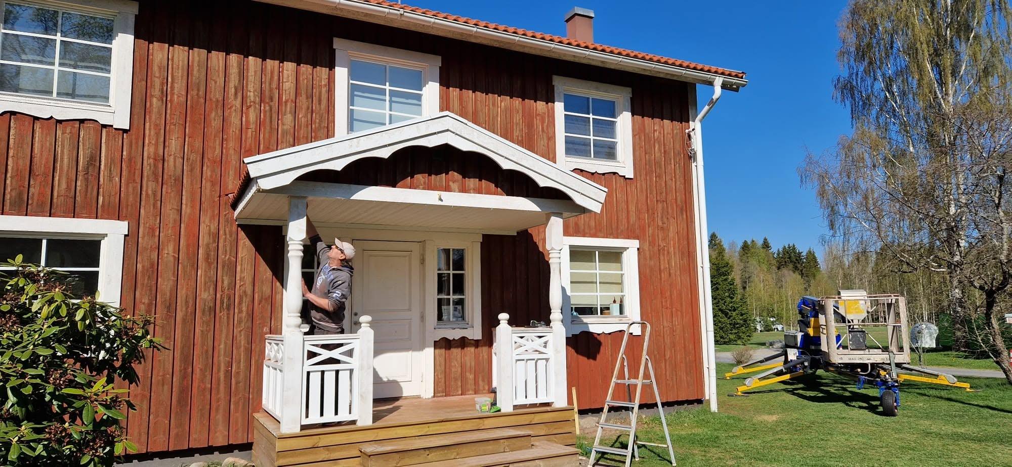 Michiel målar verandan på ett rött trähus